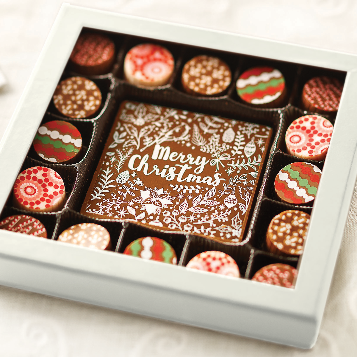 An assortment of holiday themed chocolate truffles in a box with a large center truffle decorated with holiday foliage and ornaments that says Merry Christmas.