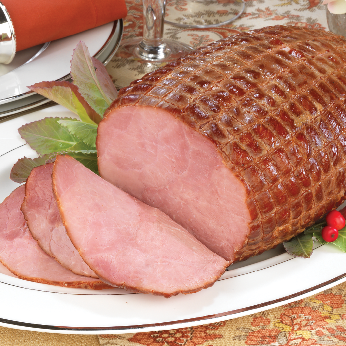 Boneless Smoked Ham with a few slices cut out, sitting on a plate and a Fall themed table setting.