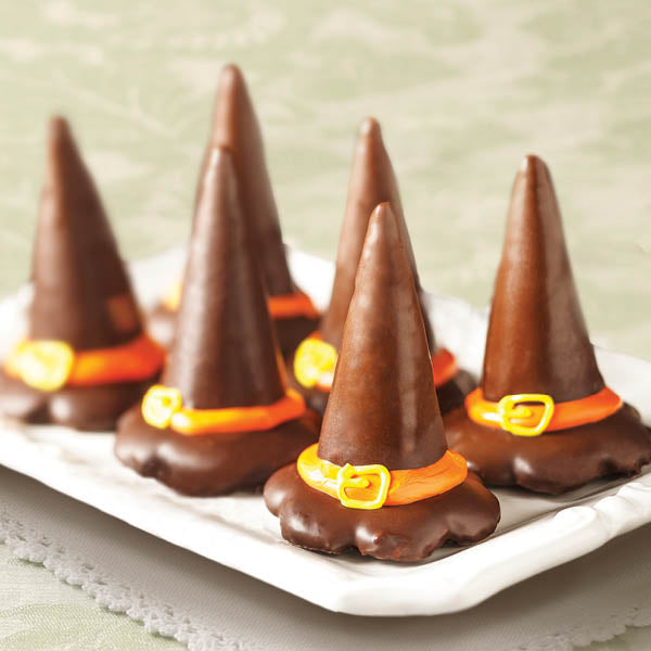 Chocolate witch hats with orange belts on a white plate against a light green background
