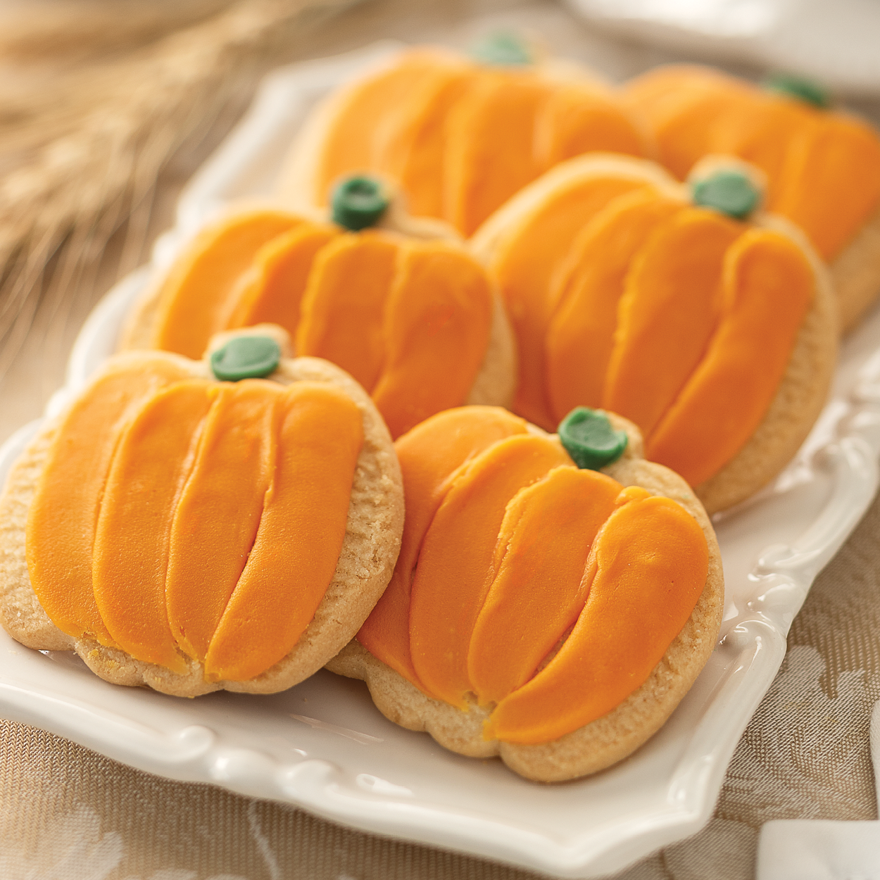 Six Pumpkin Frosted Cookies on a tray with an Autumn themed table cloth