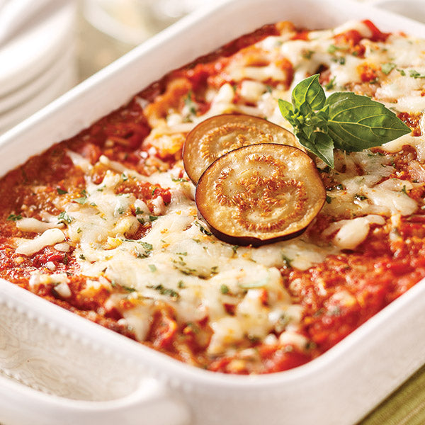 Eggplant parmesan with melted cheese, two slices of eggplant, and garnish on top. Served on a white casserole dish with handles.